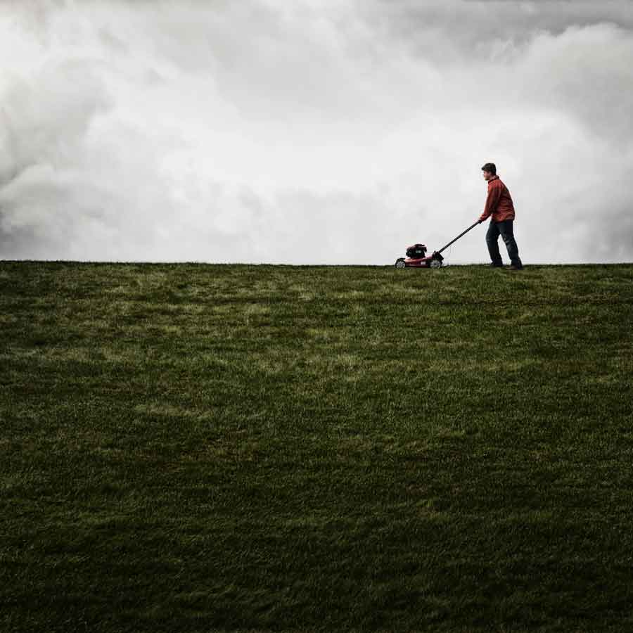 Fotografía de un hombre joven con una cortadora de césped, cortando una enorme zona de hierba.